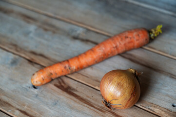 Raw, unpeeled vegetables against a wooden background. Ripe carrots and onions in a brown rind. Selective focus