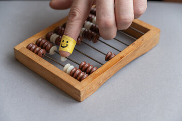 The accountant makes calculations on small wooden abacus. The man's index finger is wrapped in yellow tape. A happy smiling face is drawn on the finger. Positive emotion concept.