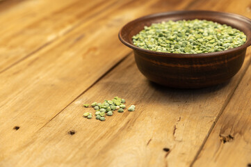 Dry split peas in a bowl against a wooden background. Green pea beans in brown earthenware bowl. Uncooked food. Healthy food. Close-up. Selective focus. Copy space for text and design elements.