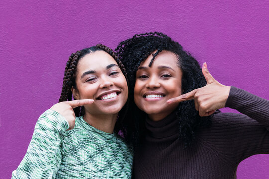 Happy friends pointing fingers at each other in front of purple wall