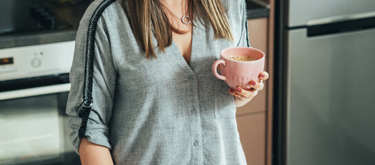 An anonymous businesswoman drinking coffee while standing in the kitchen