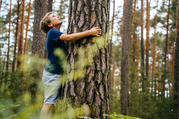 Cute pretten boy hugging a tree, looking up. connecting with nature concept.