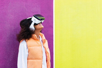 Girl wearing virtual reality simulator standing in front of yellow and purple wall