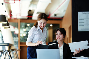 A portrait of two young Asian businesswoman using their tablet computers with calculators and documents to plan marketing strategies and investments to profit from their clients.