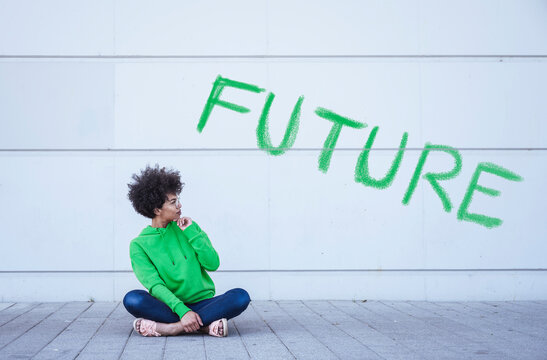 Woman sitting cross-legged on ground in front of green word Future