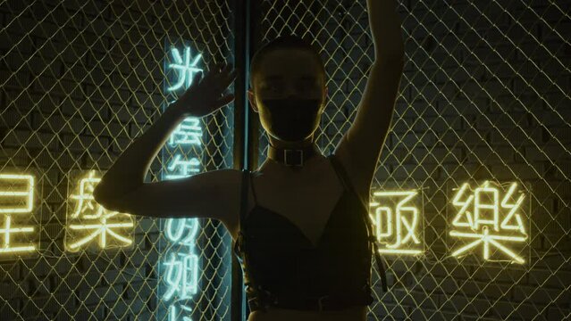 Waist-up of girl with shaved head with black paint on face moving hands and body in studio with neon lights in shapes of hieroglyphs meaning nirvana and western paradise, lights twitching