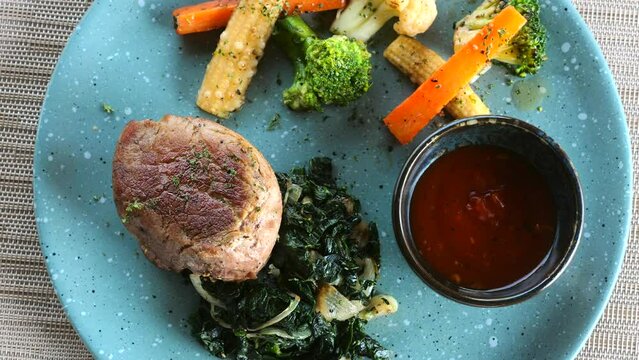 Top view of roasted beef steak with spinach and vegetables. Healthy meal with roasted meat and broccoli on blue plate in restaurant. Keto or paleo diet.
