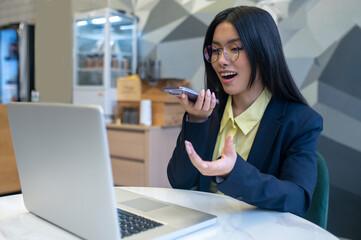 Woman talking into smartphone sitting at laptop