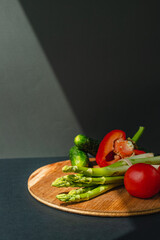 Vegetables lie on a wooden board: tomatoes, asparagus, cucumbers, red bell peppers. brown, dark gray background. place for text.