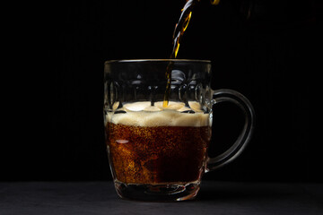 Beer is poured into a glass on a black background. A glass of dark beer. alcoholic drink
