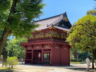 Colorful “Romon” two story high tower gate of “Nezu” shrine with zen garden pond bridge in the back as entry, beautiful summer sunlight and historic scenery with people, year 2022 June 28th