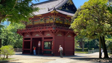 Colorful &ldquo;Romon&rdquo; two story high tower gate of &ldquo;Nezu&rdquo; shrine with zen garden pond bridge in the back as entry, beautiful summer sunlight and historic scenery with people, year 2022 June 28th