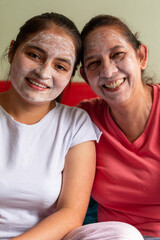 Vertical portrait of two latin women laughing and using a moisturizing mask for facial skin care. Personal care incorporating the concept. Dermatological cleansing at home.