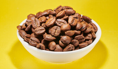 Roasted coffee beans in bowl isolated close up on yellow background, clipping path