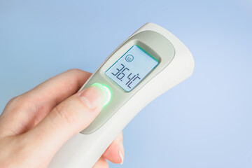 Female hand holding a modern infrared thermometer isolated over blue background