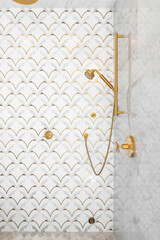 A beautiful tiled shower with gold and white tiles on the walls, mosaic marble tiles on the floor, and gold shower head and hardware.