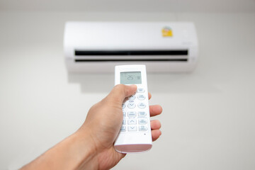 Air conditioner inside the room with close up man hand holding using directed operating remote controller to turn on and adjust the air conditioner in a room.