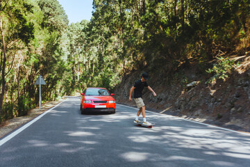 Young people having fun in the woods, skating in the middle of the road during summer
