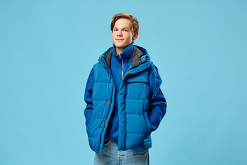 Naklejka premium a young man dressed in a fashionable blue warm vest posing on a light blue background with empty space for text