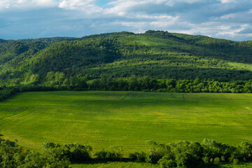 Fototapeta na wymiar Green scene with a distant mountain range and agricultural field in the foreground. Landscape photography. Summer vacations in countryside