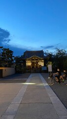 serene and modest temple house beside the main pagoda, lit with golden light from the japanese paper lanterns on the other side, blue vivid blue beautiful sky of Tokyo and the clouds.  year 2022 6/25