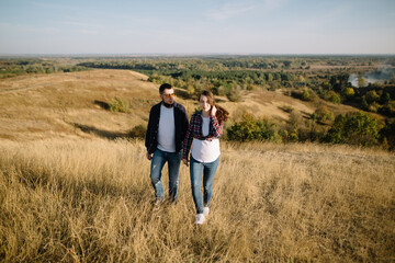 A couple of parents-to-be on a walk in the countryside in the fall. The expectant young mother walks hand in hand with future father and smiles in ordinary casual clothes. Happy motherhood and