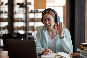 Attractive happy young student studying online at home, using laptop computer, headphones, having video chat, waving. Remote work, distance education. Video conference or virtual event on quarantine