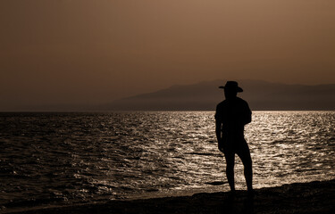 Silhouette of adult man in hat on beach during sunset