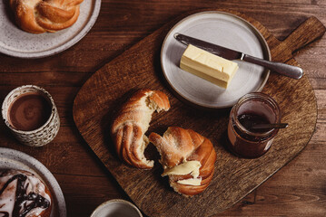 Freshly baked cardamom knot buns (also sweet rolls or swirl buns) with cocoa mug and butter and jam...