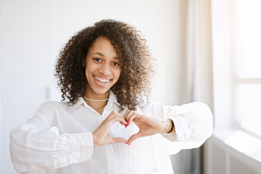 Beautiful nice pretty African american girl with her brunette curly hair she show heart symbol 