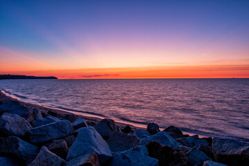Niesamowity zachód słońca nad morzem. Fale uderzające o kamienne głazy na brzegu plaży
