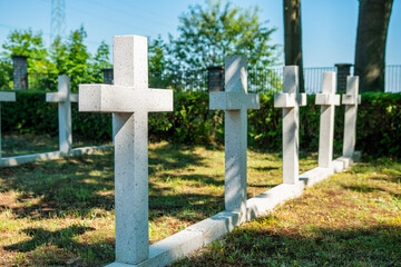 Białe, betonowe krzyże na niewielkim cmentarzu. Anonimowe groby, mogiły w świetle słonecznym