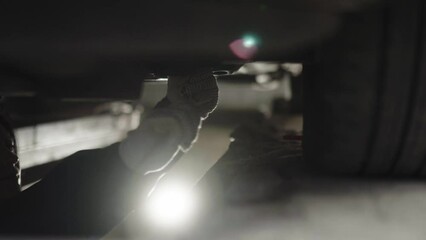 Young woman car mechanic wearing gloves working under the car in a car service, workshop. Empowering the woman in technical occupations.