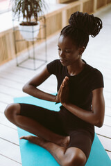 Calm and spiritual young dark skin woman with hands in namaste Asana pose, sitting in lotus...