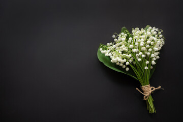 Lily of the valley flowers isolated on black background. Beautiful bouquet of white flowers with green leaves. Top view, free space, card for women's day, mother's day