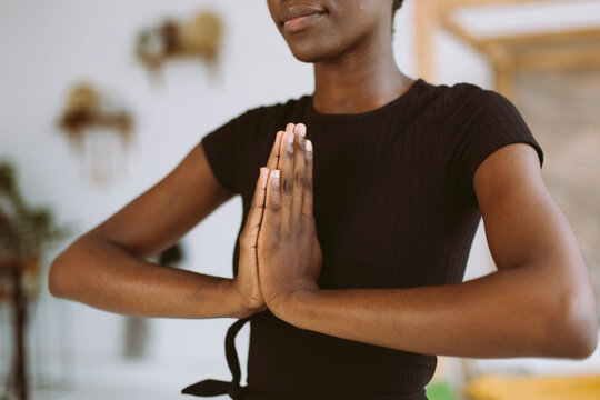 Cropped closeup and meditating young African American woman in black sportswear practicing yoga exercises, standing, keeping hands in namaste asana position. Fitness at home, relaxing. Hope and love