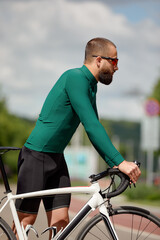 Fototapeta premium Portrait of a sporty man in a cycling outfit standing with a bicycle on the Bike Lane, posing for the camera