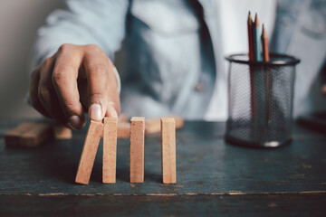 Businessman hand protecting wooden domino concept of business risk planning Fight goals for success
