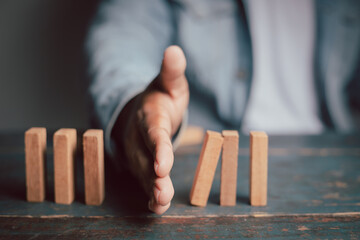 Businessman hand protecting wooden domino concept of business risk planning Fight goals for success
