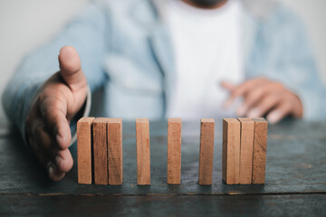Businessman hand protecting wooden domino concept of business risk planning Fight goals for success
