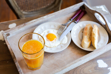 Breakfast theme. A glass of orange juice and a fried egg with toast are on a wooden tray on the table. Retro style.