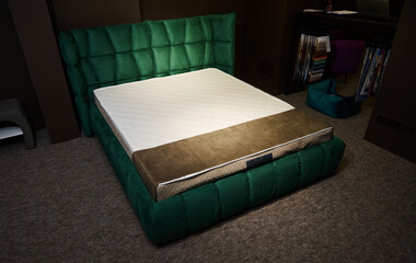 Sleeping bed made of emerald green velour upholstery with orthopedic mattress displayed for sale in furniture store. Bedroom and home interior design
