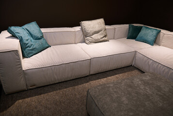 Partial view of hug comfortable beige sofa with bright green cushions displayed for sale in a furniture design studio. Home interior design concept