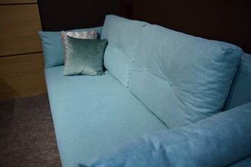 Cropped view of a comfortable minimalist stylish turquoise sofa with patterned cushions in the furniture store exposition center. Home design studio
