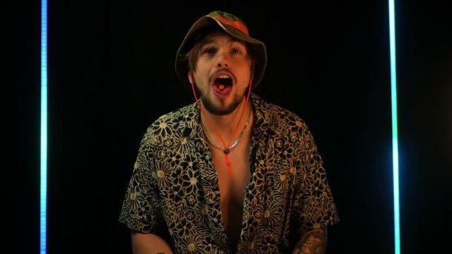 Portrait of partying dude in bucket hat putting ecstasy pill on tongue and swallowing. Grooving man in club taking disco biscuit and happily dancing. Concept of having fun with forbidden substances 
