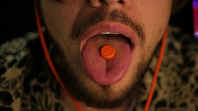 Slow mo cinematographic shot of bearded man eating bright orange disco pill. Close up of man putting ecstasy pill on tongue and swallowing it. Concept of partying long and hard with banned tablets
