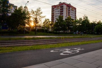 Zachód słońca w mieście. Ścieżka rowerowa, linia tramwajowa, ulica. Blokowisko.