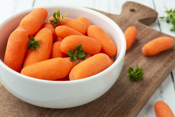 Baby carrots in a bowl over wooden table with herbs