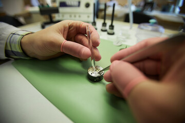Close-up of unrecognizable watchmaker in finger gloves using tweezers and lubricating watch movement