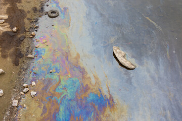 Industrial debris and colored stains of gasoline or oil on the water surface near the river bank. Concept ecological problems and environmental pollution. - obrazy, fototapety, plakaty